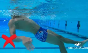 Underwater view of a swimmer demonstrating an incorrect backstroke arm movement. A red X marks the improper arm position.