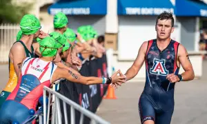 A male NCAA triathlon athlete in a dark blue and red suit with an "A" logo high-fives a competitor.