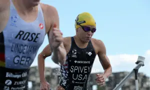 Taylor Spivey, a triathlete in a yellow cap and goggles, emerges from the water, her USA suit glistening.