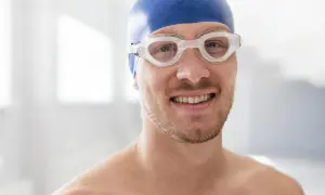 A smiling man in a blue swim cap and goggles, ready to swim. He's wondering, "When can I swim after wisdom teeth removal?