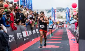 A determined runner approaches the Ironman finish line, cheered on by a crowd.