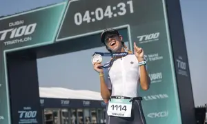 Caroline celebrates her finish at the Dubai T100 Triathlon, medal in hand, under the finish arch.