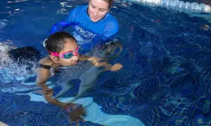 A swim instructor guides a young girl learning to swim. The question of how long does it take to learn how to swim varies, but with practice, she'll be swimming confidently.