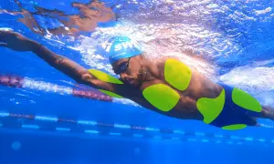A swimmer's body, with neon green highlights on their torso and arms, glides through a blue pool.