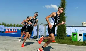 Athletes in racing gear push forward during a triathlon training run, focused and determined under a bright blue sky.