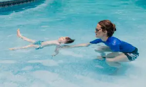 A child floats on their back in a pool during ISR swim lessons, with an instructor reaching out to support them.