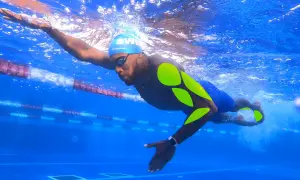 Swimmer in blue cap and goggles, with neon green markings on his body, powerfully pulls through the water in a lane.