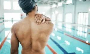 Swimmer holding shoulder in pain, questioning if you can swim with a torn rotator cuff.