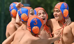 A group of young water polo players, wearing orange and blue caps with numbers, celebrate a victory. One boy, with a big smile, shouts "Habawaba!