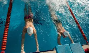 Two swimmers practice their flutter kicks, pushing off the wall in a race.