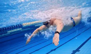 Swimmer executing a powerful butterfly stroke underwater, creating a splash as they propel through the blue pool lanes.