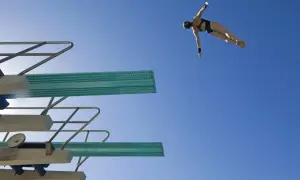A diver in mid-air, performing a competitive dive against a clear blue sky.