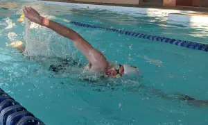 Swimmer pushing hard in a pool, arms extended, water splashing. This intense effort is part of a challenging vo2 max workout.