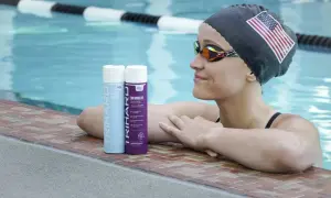 Swimmer with an American flag cap and goggles rests by the pool, with TRIHARD swimmer's shampoo bottles nearby, offering a solution on how to protect skin from chlorine.