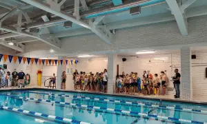 Children in swimsuits gather by the pool at Jim Montgomery Swim School, ready for lessons.