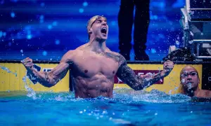 A triumphant swimmer, showcasing why swimmers have broad shoulders, celebrates in the water.