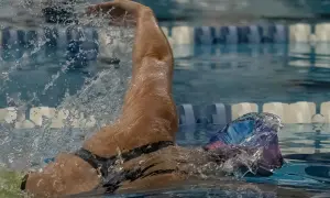 A swimmer's arm slices through the water, demonstrating the powerful stroke needed to swim laps. Water splashes around them as they focus on their technique.