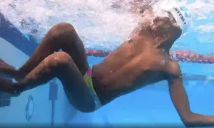 Underwater view of a swimmer performing a breast stroke, with arms extended forward and legs bent, showing the technique.