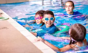 Children enjoy swim lesson games, splashing and laughing in the pool with goggles and flotation devices.