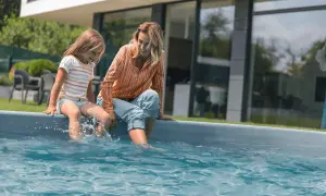 A mother and daughter sit by a pool, splashing their feet. They're enjoying a sunny day, and the daughter asks, "Can you swim with mono?