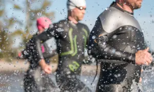 Triathletes in Ironman wetsuits run through water, splashes obscuring the view. Following Ironman wetsuit rules, they prepare for the race.