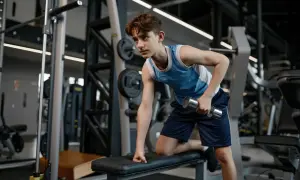 Young swimmer performing dumbbell rows as part of their cross training routine in a gym.