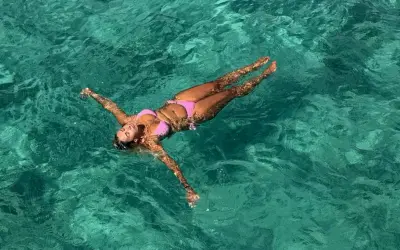 A woman in a pink bikini floats on her back in clear turquoise water. She's enjoying the water, and yes, you can swim with a tampon.