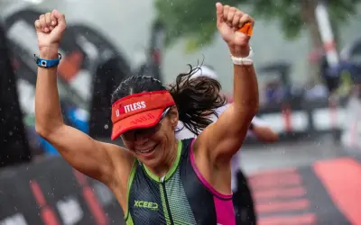 A triumphant athlete celebrates crossing the finish line of an Ironman length race in the rain.