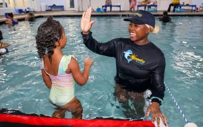 A swim instructor gives a young girl a high-five during swim stroke lessons.