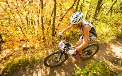 Athlete races through an autumn forest during an off road triathlon, navigating a dirt path with colorful foliage.
