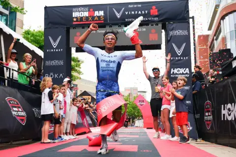 A triumphant athlete breaks the tape at the Memorial Hermann Ironman Texas, celebrating a victory in this demanding team triathlon event.