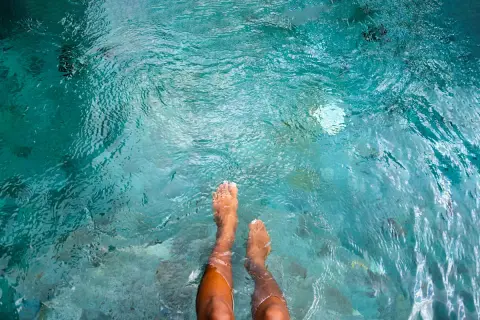 Feet submerged in clear turquoise water, with small fish swimming around. A person wonders if they can swim with a yeast infection.