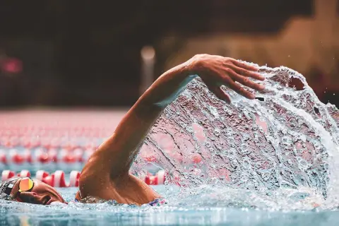 A swimmer's arm slices through the water, creating a dramatic splash during a powerful stroke. The focus is on the dynamic movement as they swim.