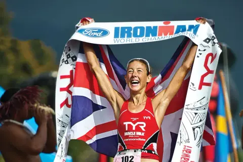 Chrissie Wellington celebrates her Ironman World Championship win, draped in the Union Jack and holding the Ford Ironman banner.