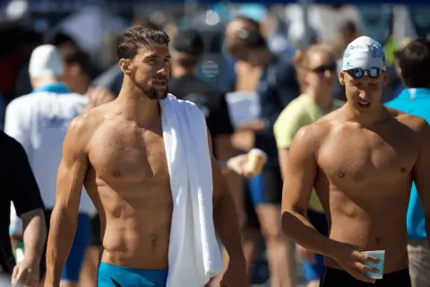 Two muscular men, one with a towel draped over his shoulder, showcase the lean physique of a swimmer body vs. a gym body.