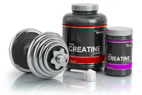 Dumbbells and containers of creatine powder and capsules, ideal for swimmers looking to boost their performance.