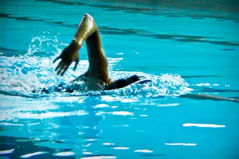 Swimmer's arm in a powerful high elbow catch, slicing through the turquoise water with a splash.