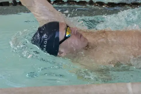 Swimmer executing a backstroke flip turn, water splashing around their head and goggles.