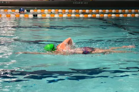 A swimmer in a green cap performs a front crawl swim, their body streamlined as they glide through the turquoise water.