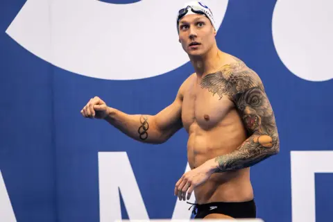 A muscular swimmer with extensive tattoos, including Olympic rings, prepares for a race, showcasing his dedication to swim conditioning.