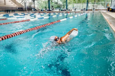 A woman enjoys a 30-minute pool workout, swimming laps in a bright blue lane.