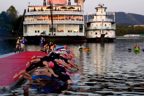 Triathletes dive into the water at 70.3 Chattanooga, with paddle boats and riverboats in the background.