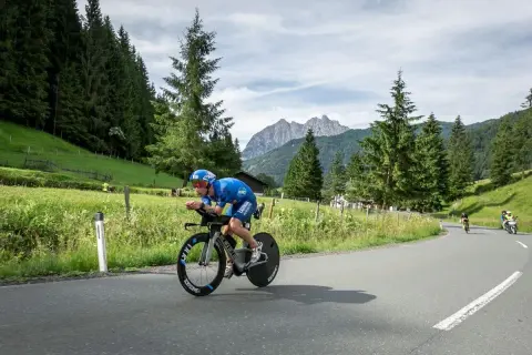 Athlete in blue cycling gear races on a road bike during a sprint triathlon, with a scenic mountain backdrop.