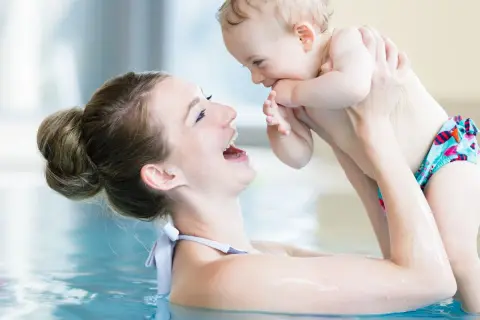 Mother and baby laughing in a pool. A happy mom asks, "When can you swim after C-section?