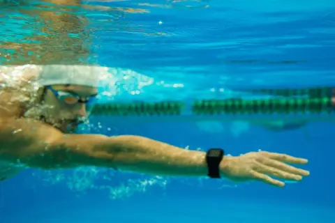 Underwater view of a swimmer in goggles and cap, focused on a long distance swim, with a smartwatch on their wrist tracking progress.