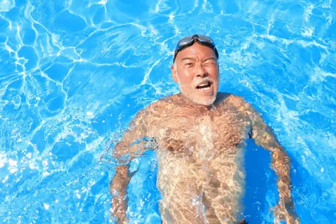 Man in pool, goggles on, with a surprised expression, experiencing immersion diuresis.