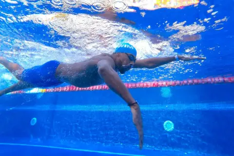 Swimmer in blue cap and goggles glides through the water, a powerful stroke that can help you increase your VO2 max.