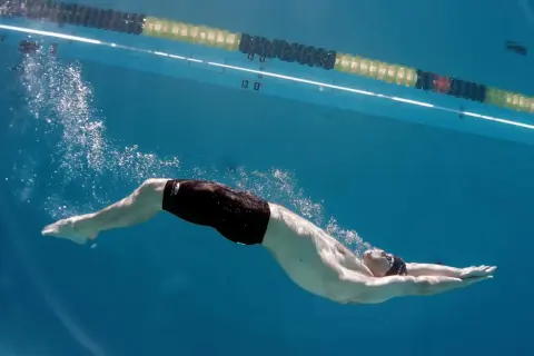 Underwater view of a swimmer performing a powerful kick, showcasing effective leg workouts for swimmers. Bubbles trail behind as they glide through the blue water.