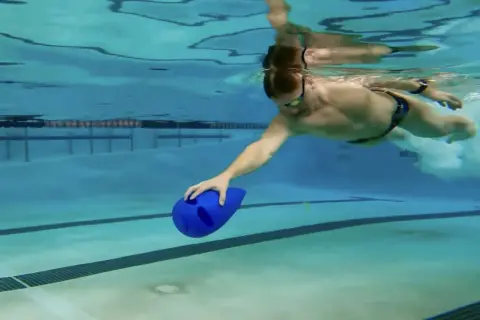 Man swimming underwater with a blue kickboard, practicing his kickboard swim technique.