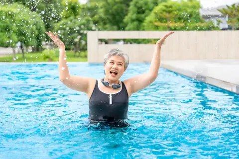Joyful senior woman splashing water in a pool, enjoying her beginner swim workout.